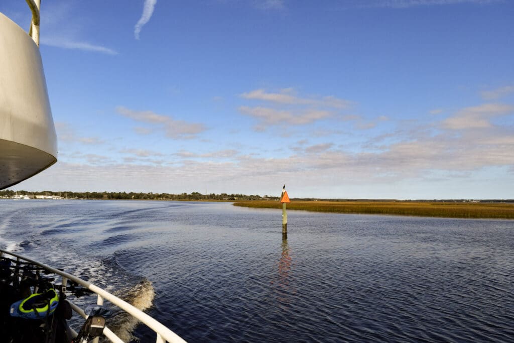 View from a boat moving through coastal Georgia's calm marsh waters with a navigation marker in the distance while traveling by ferry to Cumberland Island National Seashore
