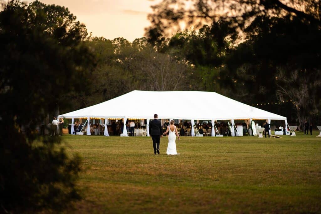 A bride and groom look towards the large white tent that holds their wedding guests on the lawn of the Horse Stamp Inn