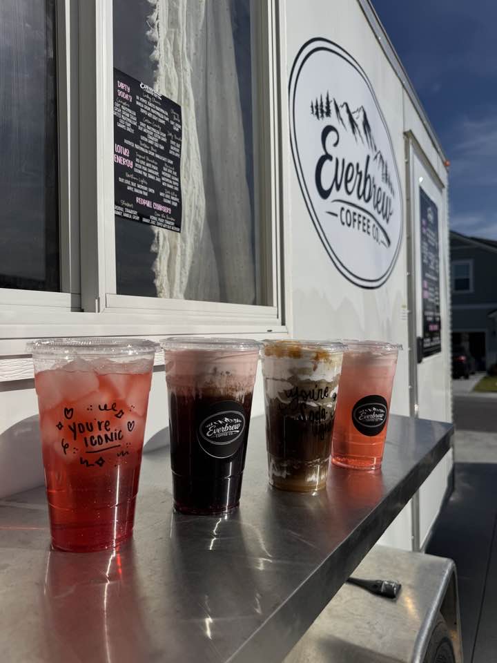 Four specialty drinks in clear plastic cups with Everbrew Coffee Co. branding sitting on and exterior stainless steel counter of a food truck.