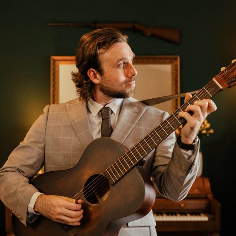 Welsh Guitarist Gareth Pearson in a jacket and tie playing and acoustic guitar