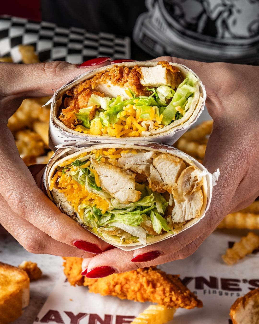 Fried chicken finger wrap cut in half and being held with open end toward camera.