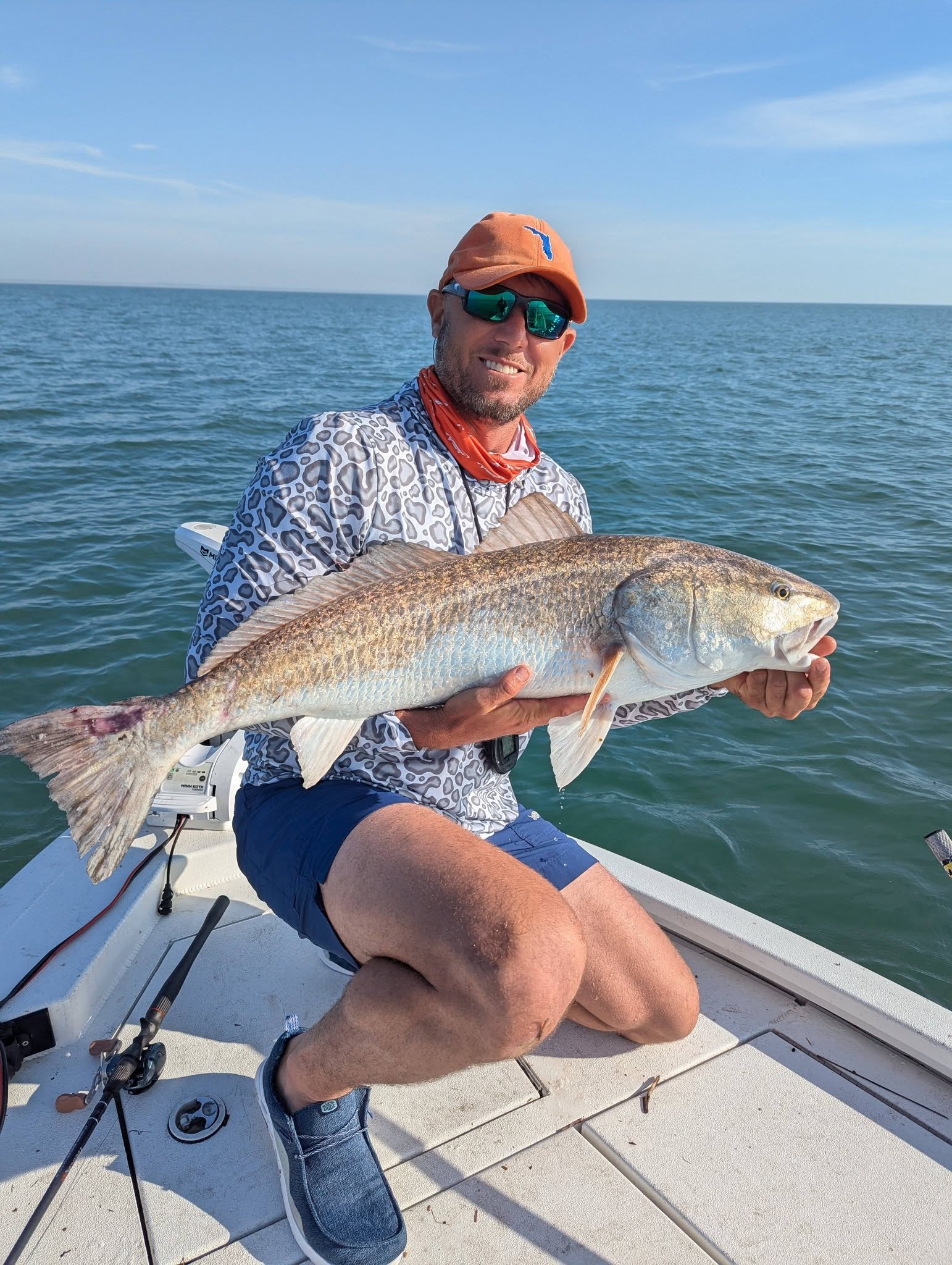 Man on a boat deck holding a large red drum fish.