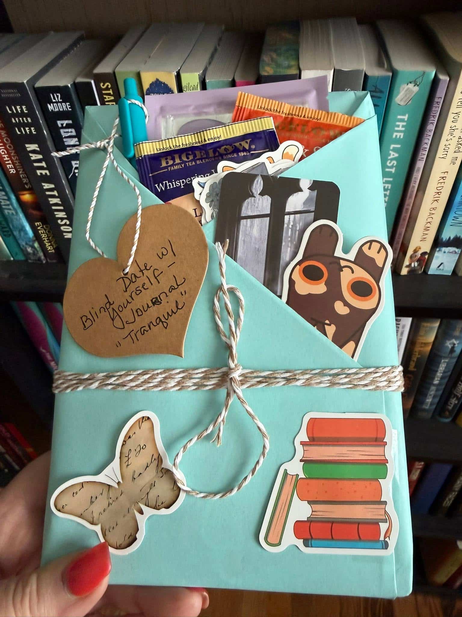 Booklovers gift bundle with bookmarks, stickers, tea bag, and more in a blue envelope wrapped with twine.