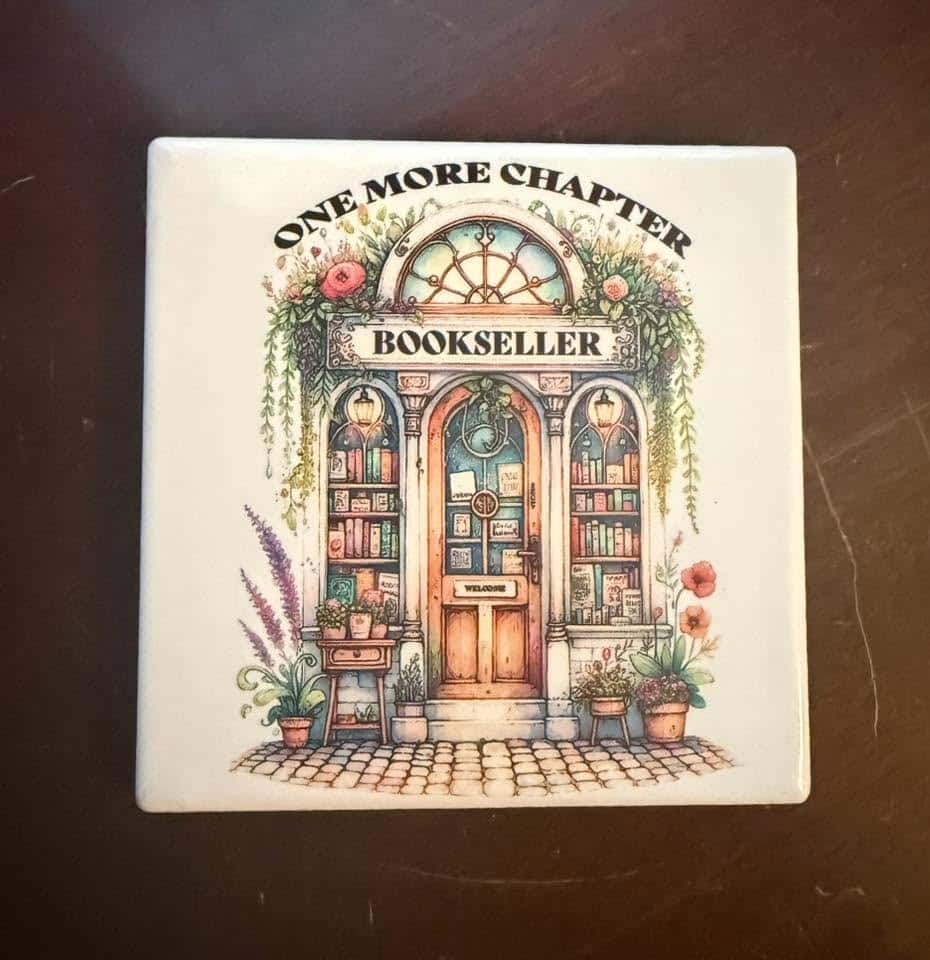 One More Chapter Bookseller Branded Ceramic Coaster with picture of front door surrounded by bookshelves on either side