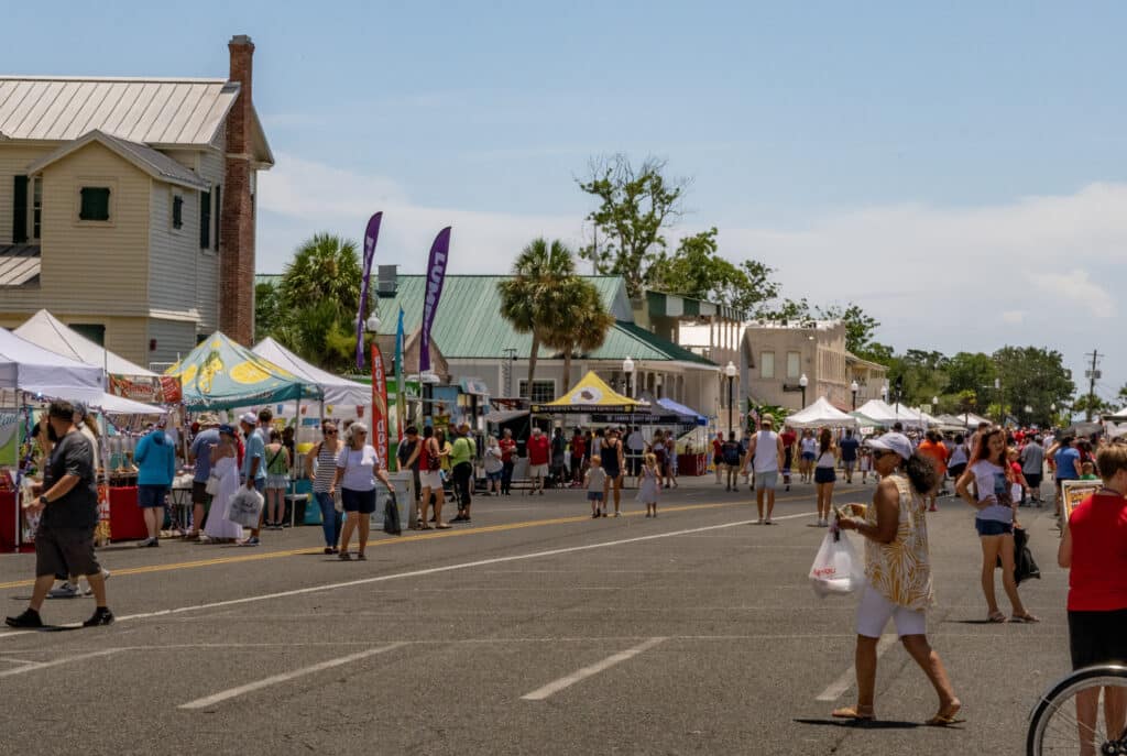 People walk along a festival lined street with food and various objects in Historic Downtown St. Marys, GA