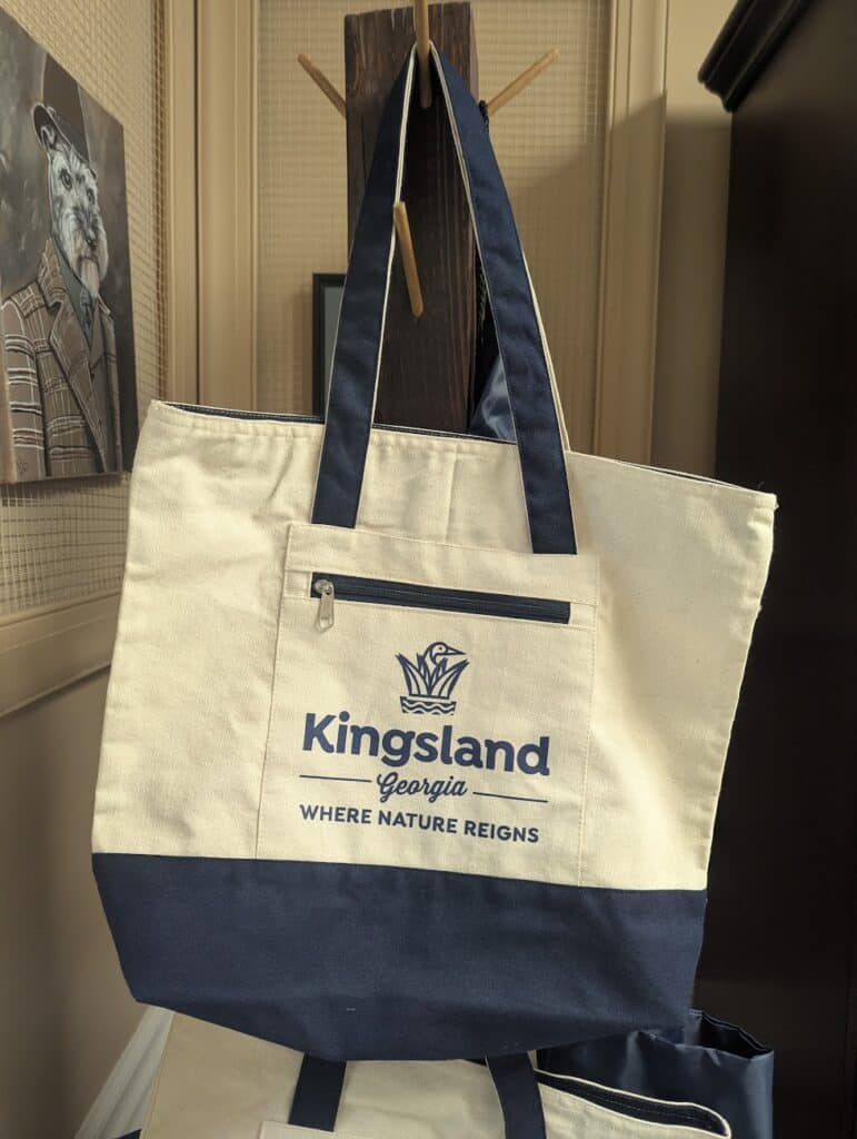 Navy blue and ivory Visit Kingsland tote bag hanging from a dark wood coat rack.