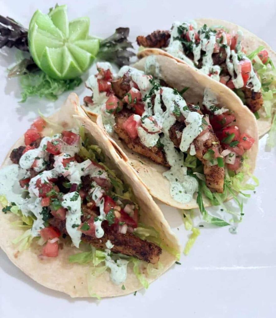 Three blackened Mahi Tacos on soft tortillas shells on a white plate with a lime garnish