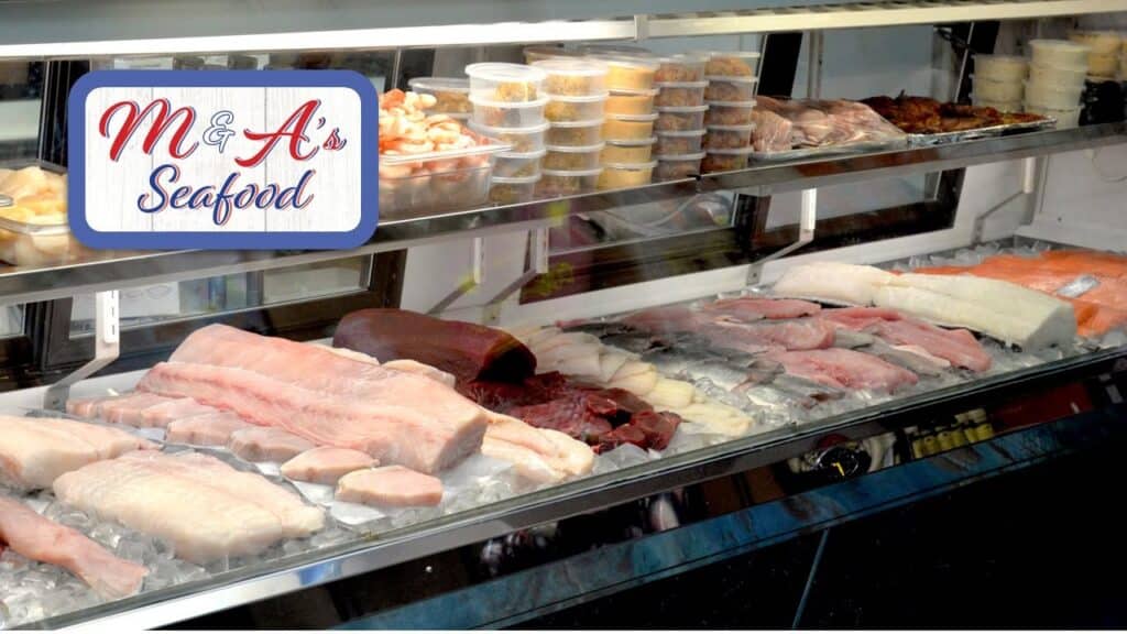 Deli counter displaying fish filets on ice with the logo for M&A's Seafood Market in the upper left of the image