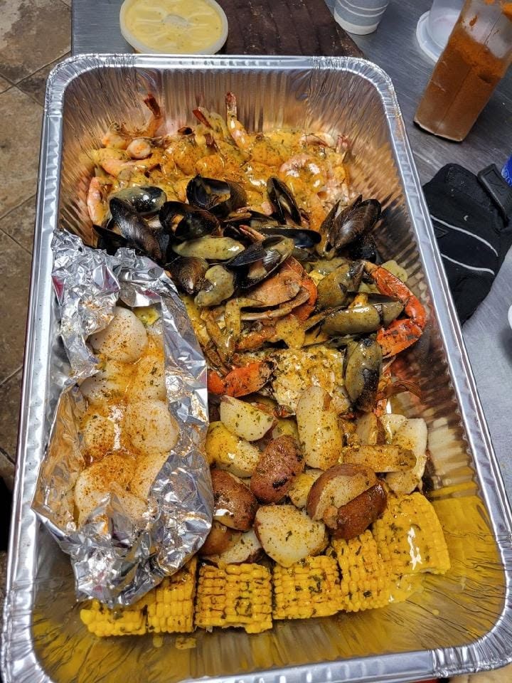 Aluminum pan with cooked ingredients for a lowcountry boil, including corn on the cob, scallops, small potatoes, mussels, and shrimp