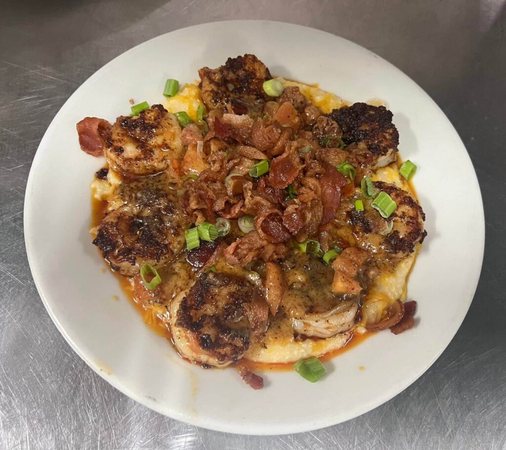 White soup bowl with blackened shrimp and grits topped with bacon bits