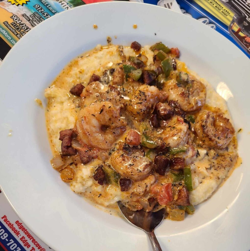 White bowl of shrimp and grits with a spoon.
