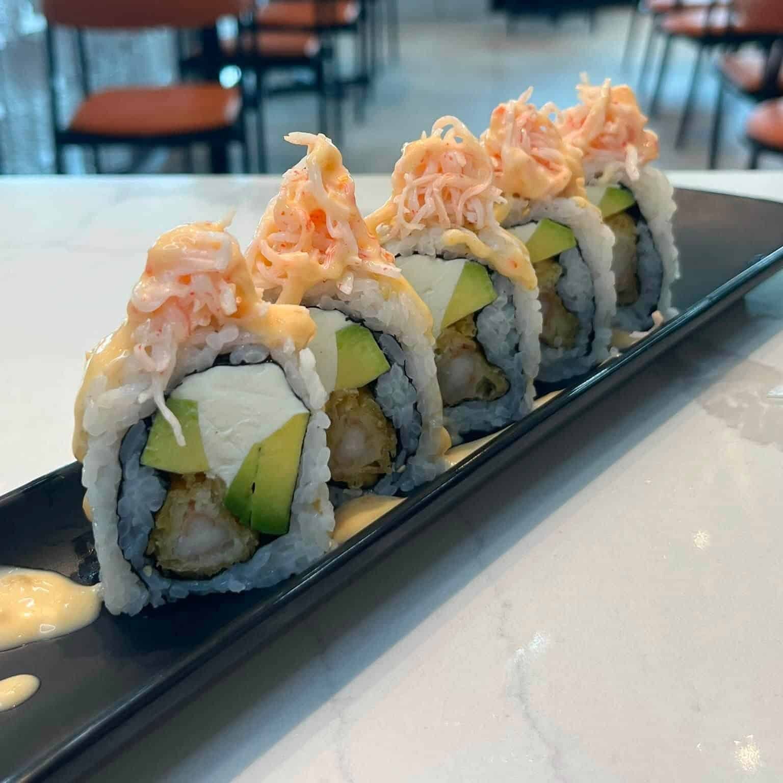 Five pieces of sushi roll topped with crab meat on a black plate.